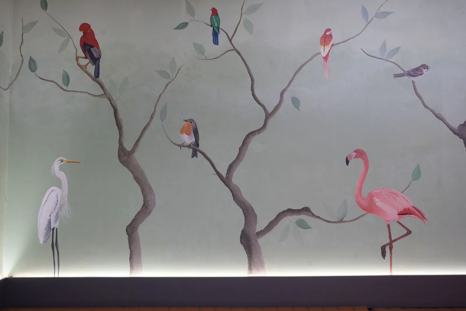 A wide stretch of the mural: an egret and a flamingo standing among painted branches, with smaller birds above