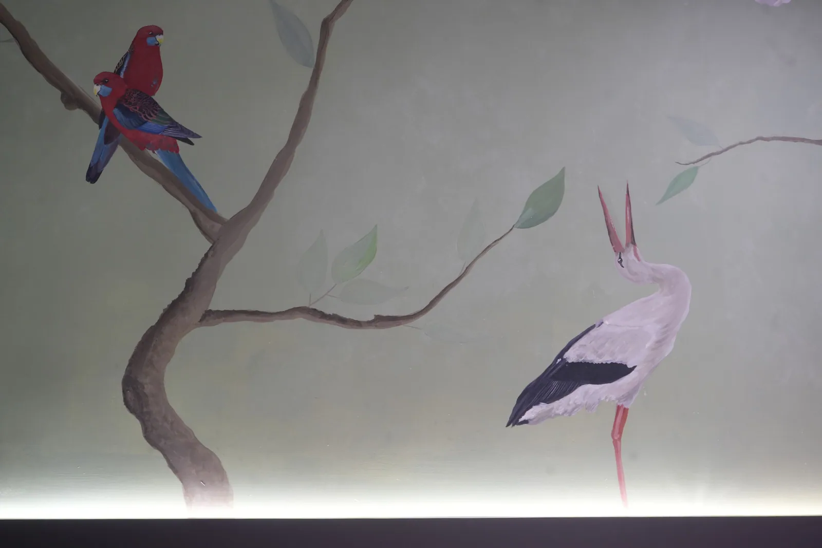 A painted crimson rosella on a branch, with a long-billed wading bird below