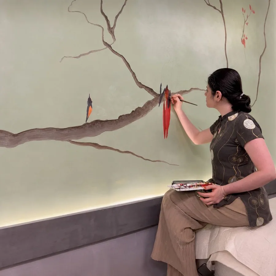 Yuvasri painting a bird directly onto a wall, palette in hand