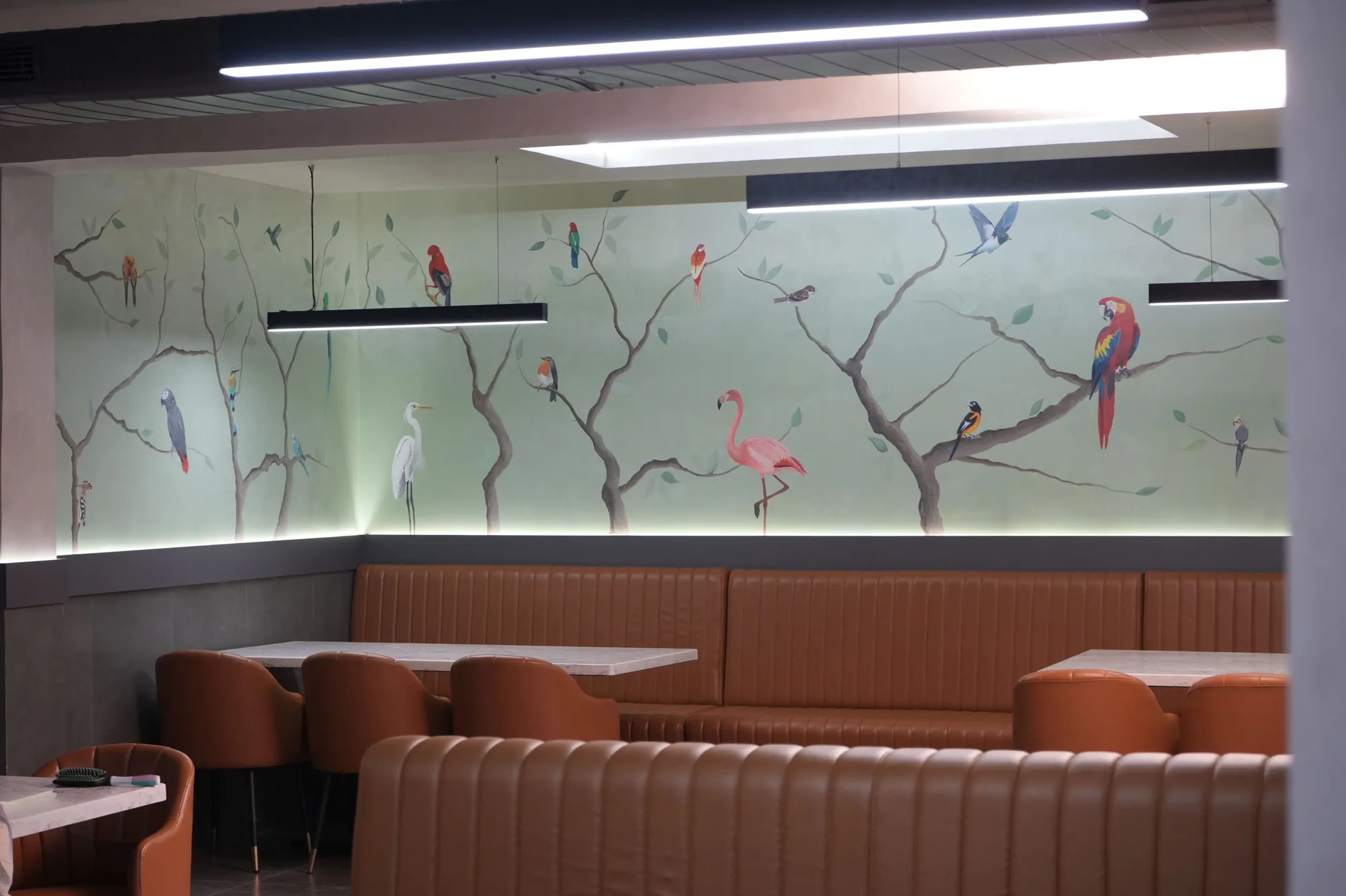 The hotel dining room, its walls painted corner to corner with birds on branches above the banquette seating