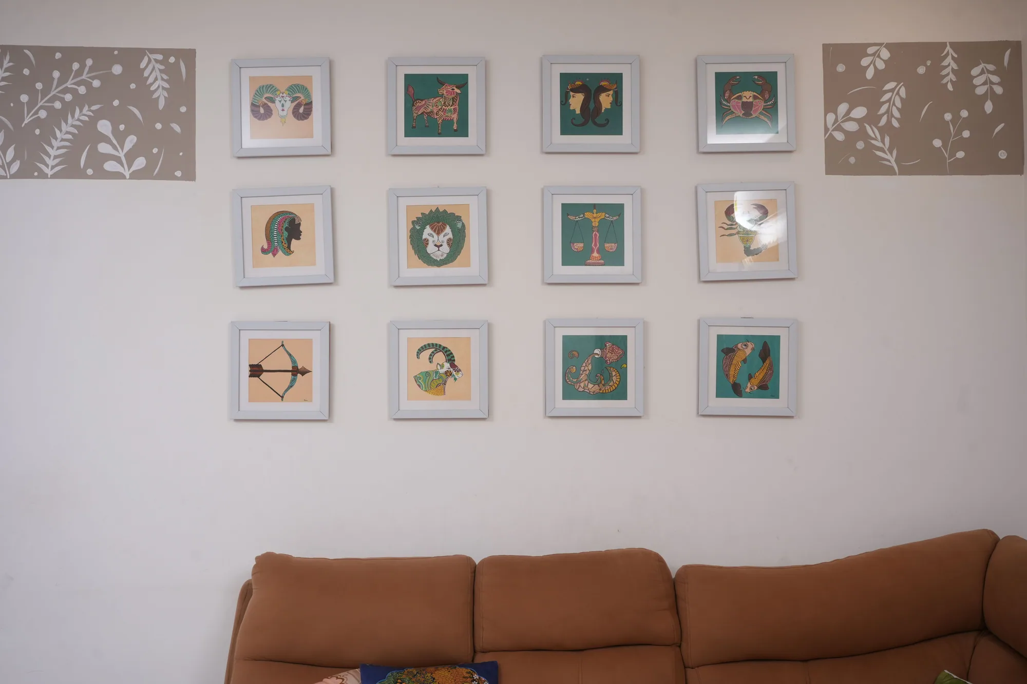 The twelve framed zodiac paintings hung together as one grid on the wall above a sofa