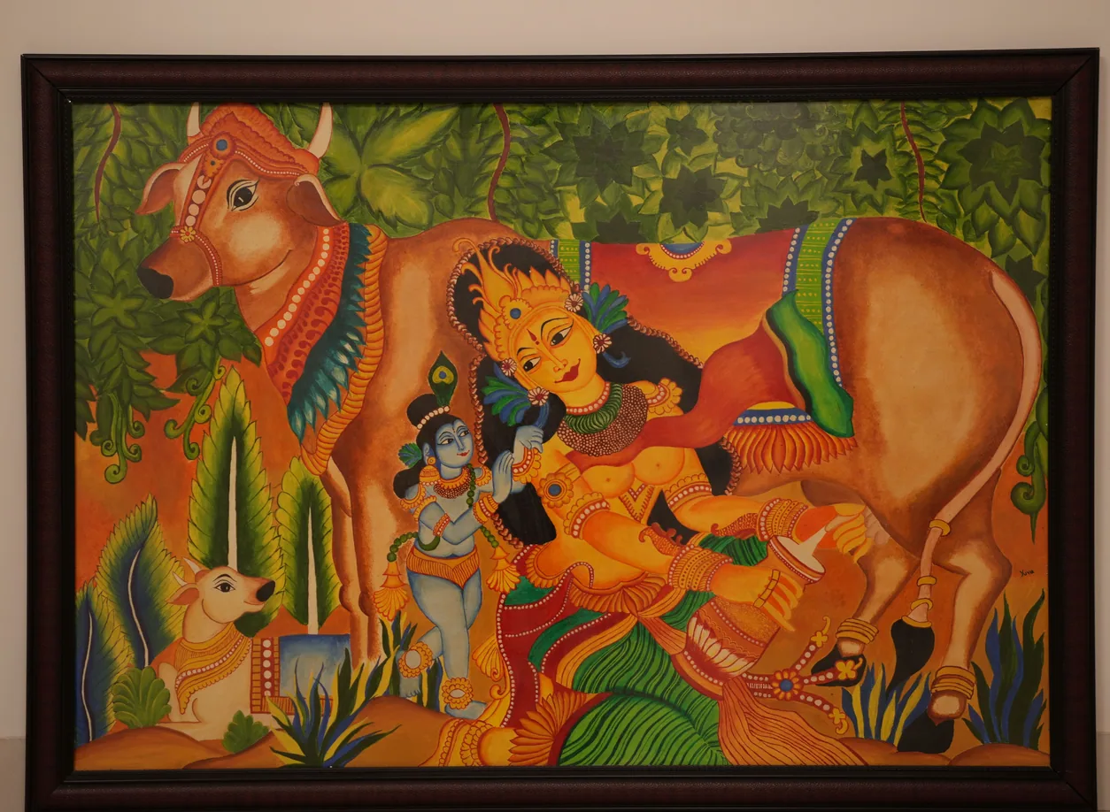 Vivid painting in the Kerala mural style of Kamadhenu, the divine cow, with Krishna and attendant figures among green foliage on an orange ground